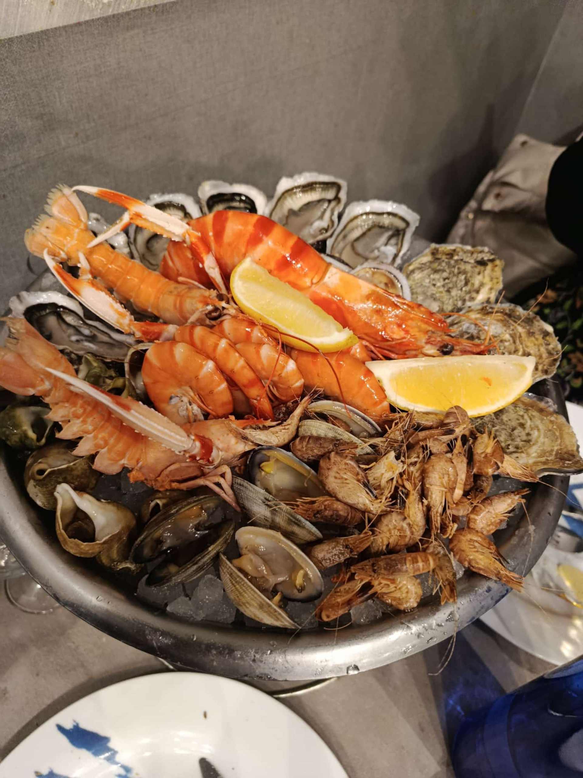 Grand plateau de fruits de mer avec un assortiment de coquillages frais, comprenant des hu&icirc;tres, des crevettes et des gambas grill&eacute;es, garnies de quartiers de citron. Les fruits de mer sont pr&eacute;sent&eacute;s sur un lit de glace, soulignant leur fra&icirc;cheur.