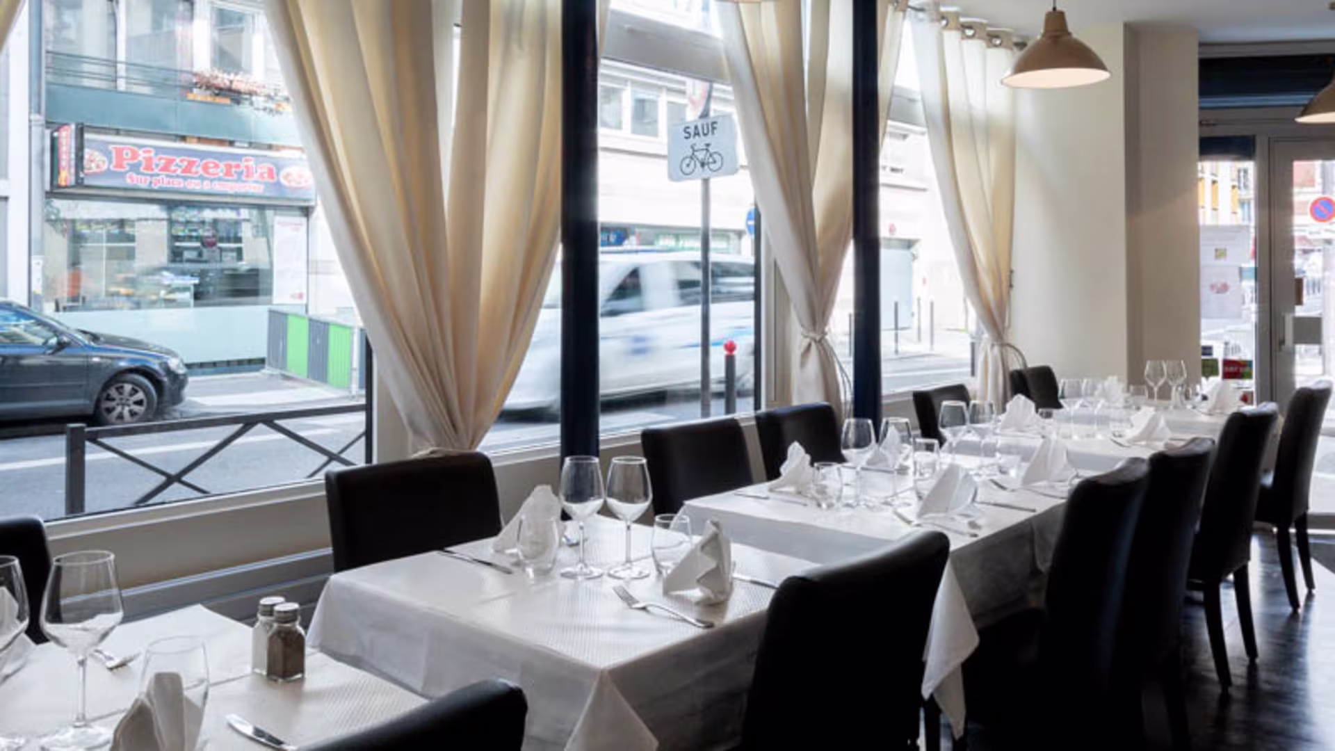 Int&eacute;rieur de restaurant soign&eacute; avec des tables couvertes de nappes blanches, &eacute;clairage doux et grandes fen&ecirc;tres laissant entrer la lumi&egrave;re naturelle, cr&eacute;ant une atmosph&egrave;re accueillante et relaxante.