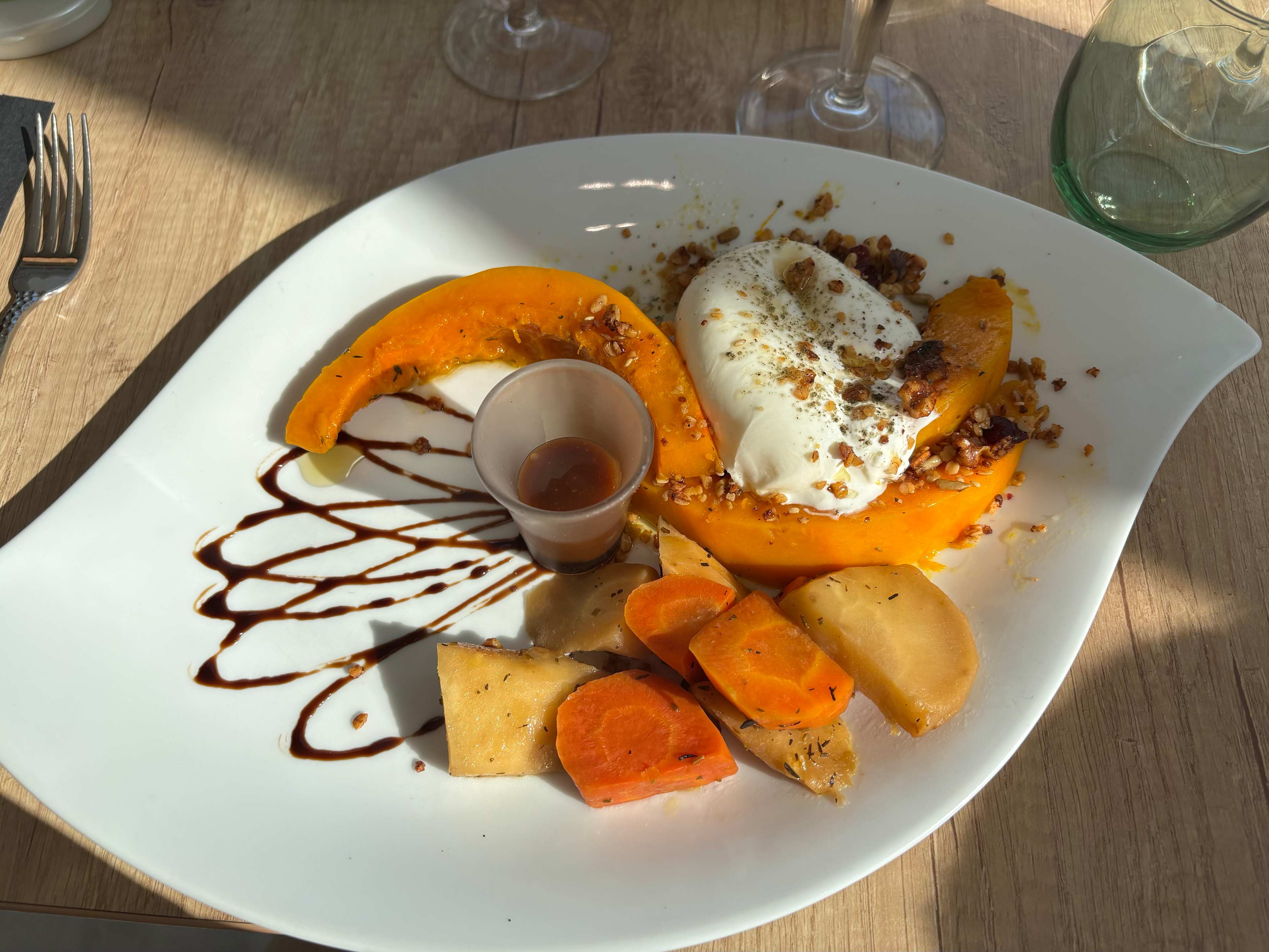 Dessert joliment présenté avec des tranches de potiron rôti doré et tendre, accompagné d'une boule de crème glacée à la vanille, parsemée de noix concassées, et d'un petit shot de sauce caramel.