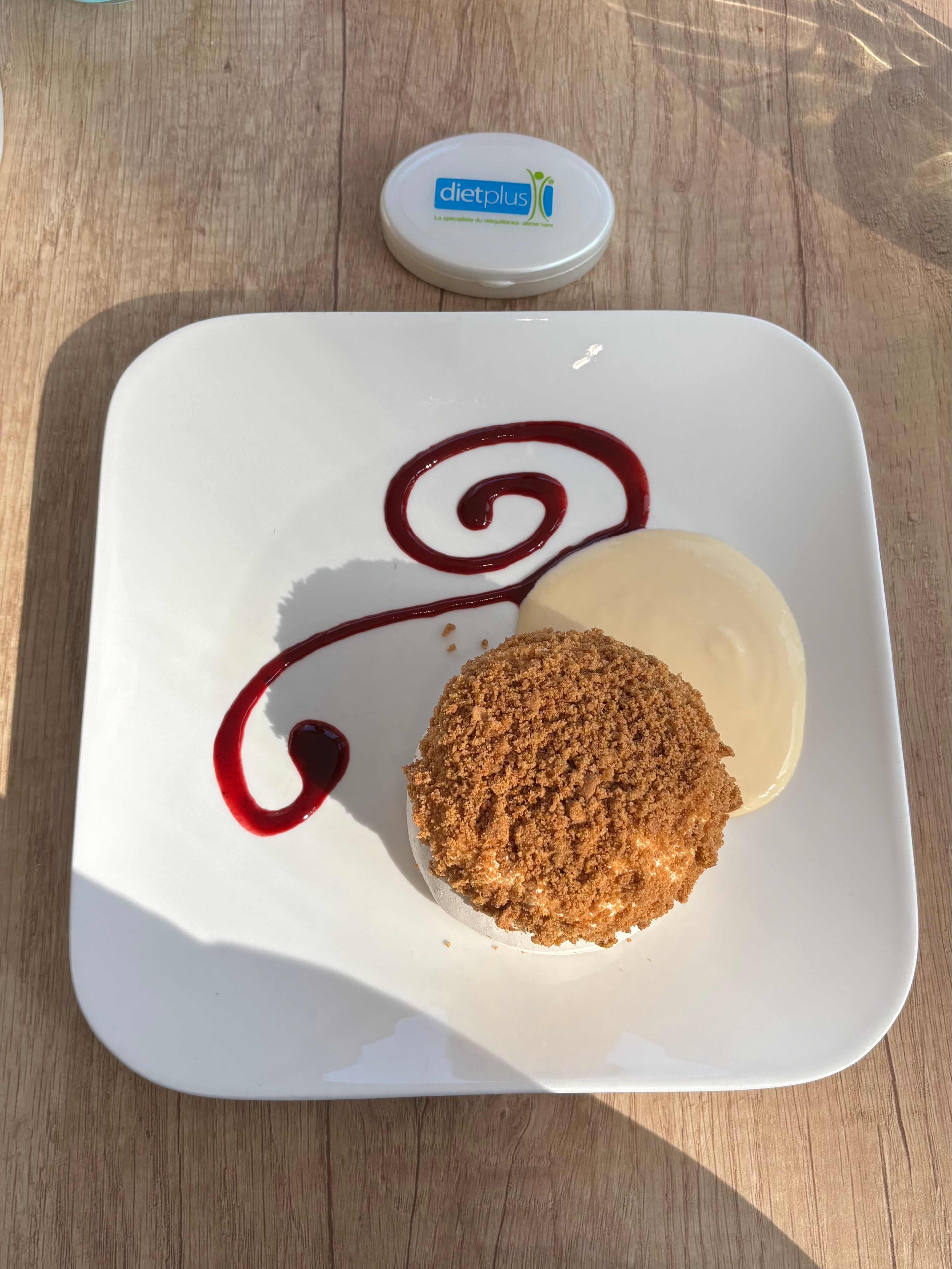 Dessert composé d'un gâteau rond et friable, surmonté d'une croûte dorée, accompagné d'une sauce crémeuse à la vanille et d'un tourbillon de sauce aux baies pour une touche colorée.