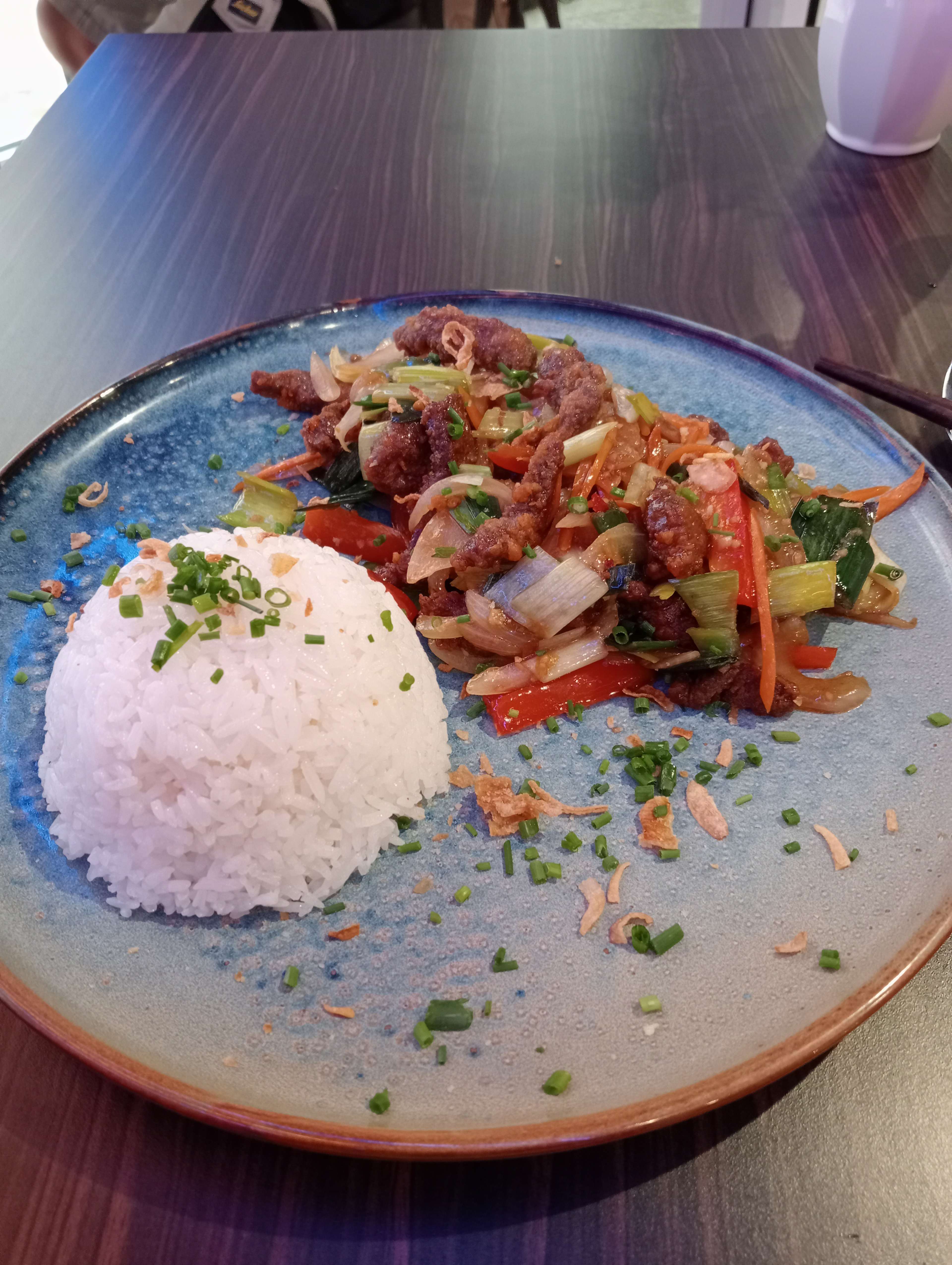 Plat coloré de lanières de bœuf sautées avec un mélange de légumes, servi avec du riz blanc moelleux et garni d'oignons verts hachés.