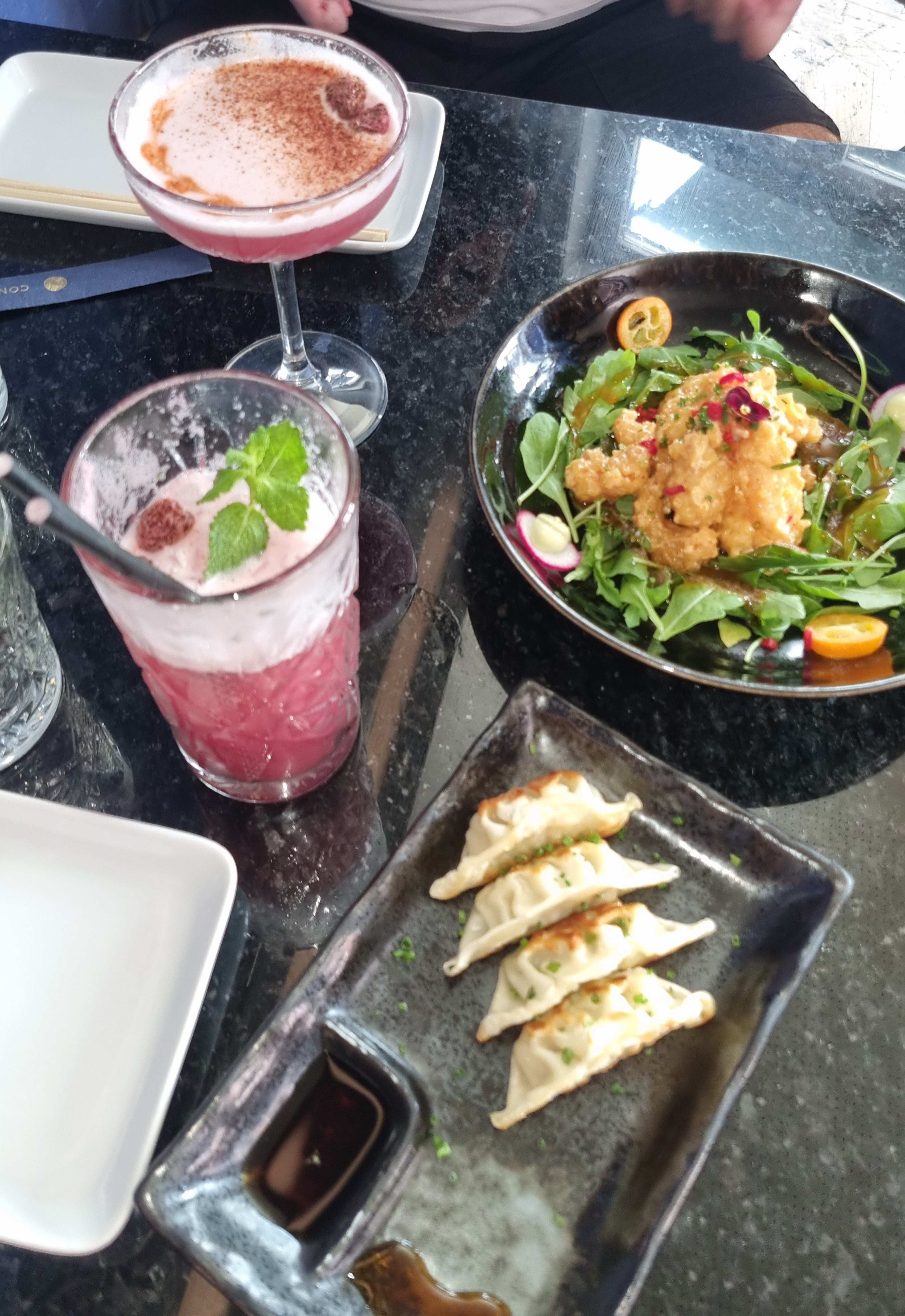Salada colorida com elementos fritos crocantes, sementes de romã e fatias de kumquat, acompanhada de dumplings levemente dourados e um molho para mergulhar.