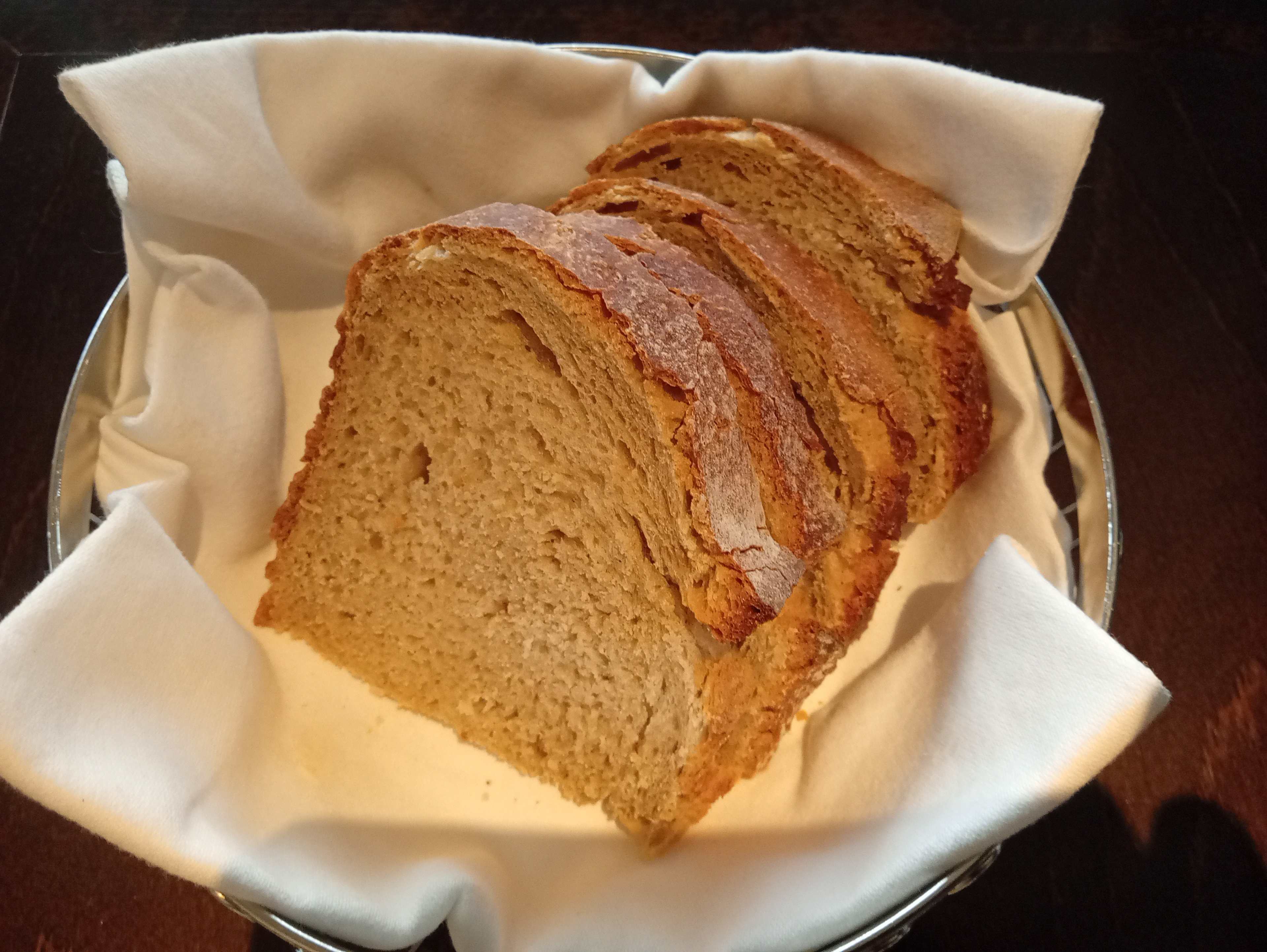 Panier de tranches de pain brun fraîchement cuit, avec une croûte dorée et une texture rustique, présentant une mie douce et moelleuse.