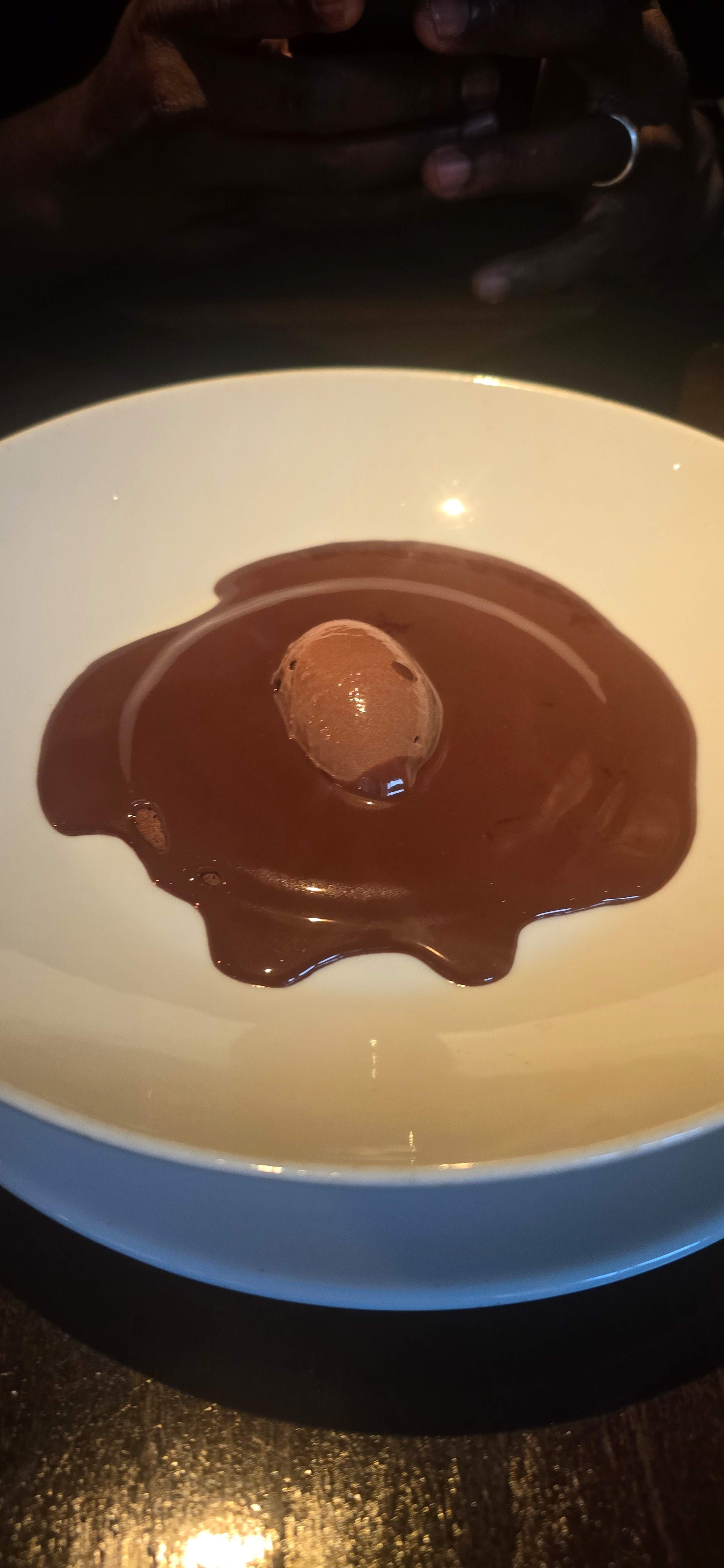 Dessert au chocolat lisse, avec une sauce au chocolat brillante entourant une mousse au chocolat au centre, offrant une présentation élégante et gourmande.