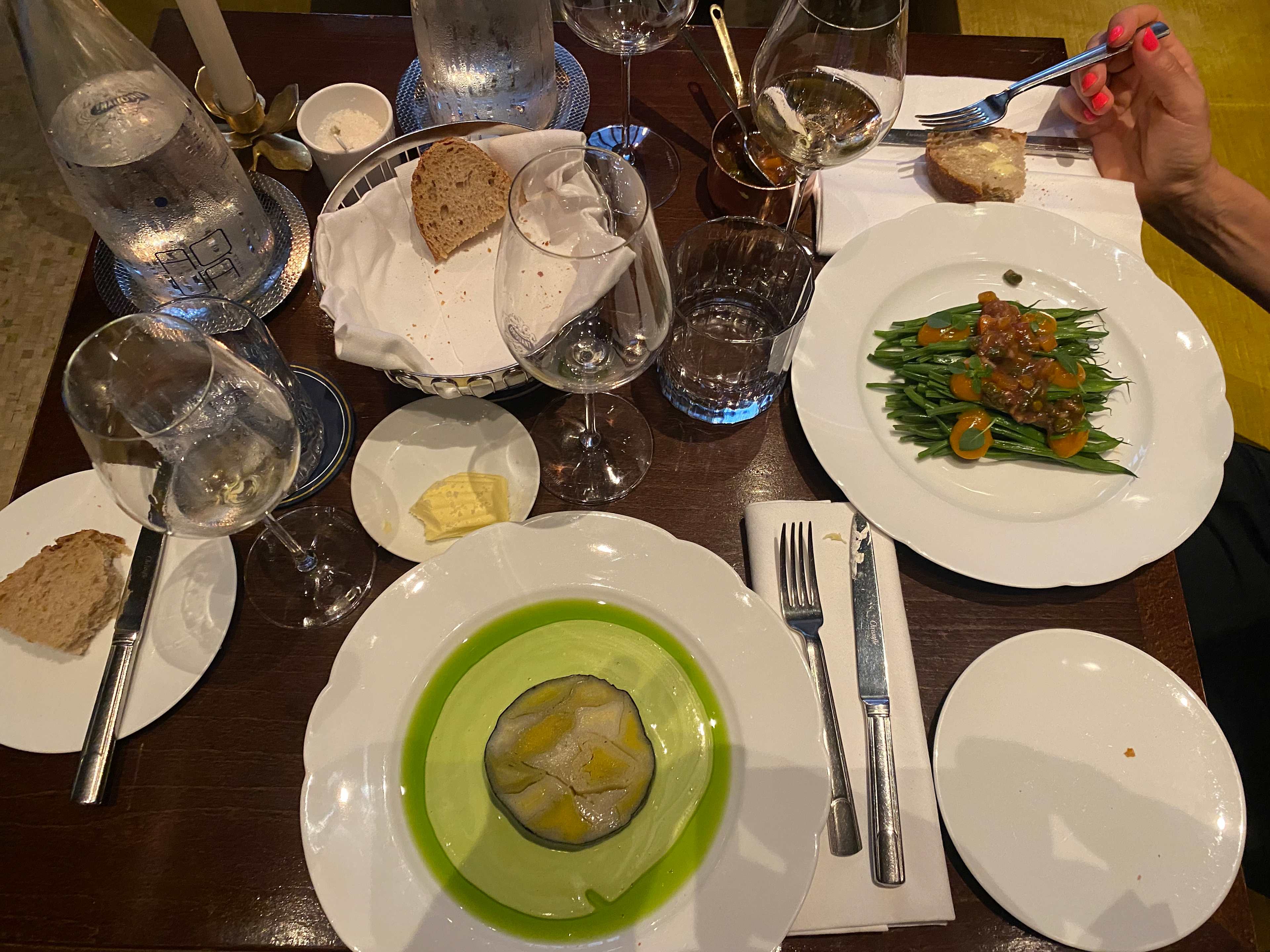 Plat joliment présenté avec une couche gélatineuse verte, probablement une aspic ou terrine, garni de tranches de légumes jaunes. Accompagné de haricots verts frais surmontés d'une sauce acidulée et de segments d'orange.