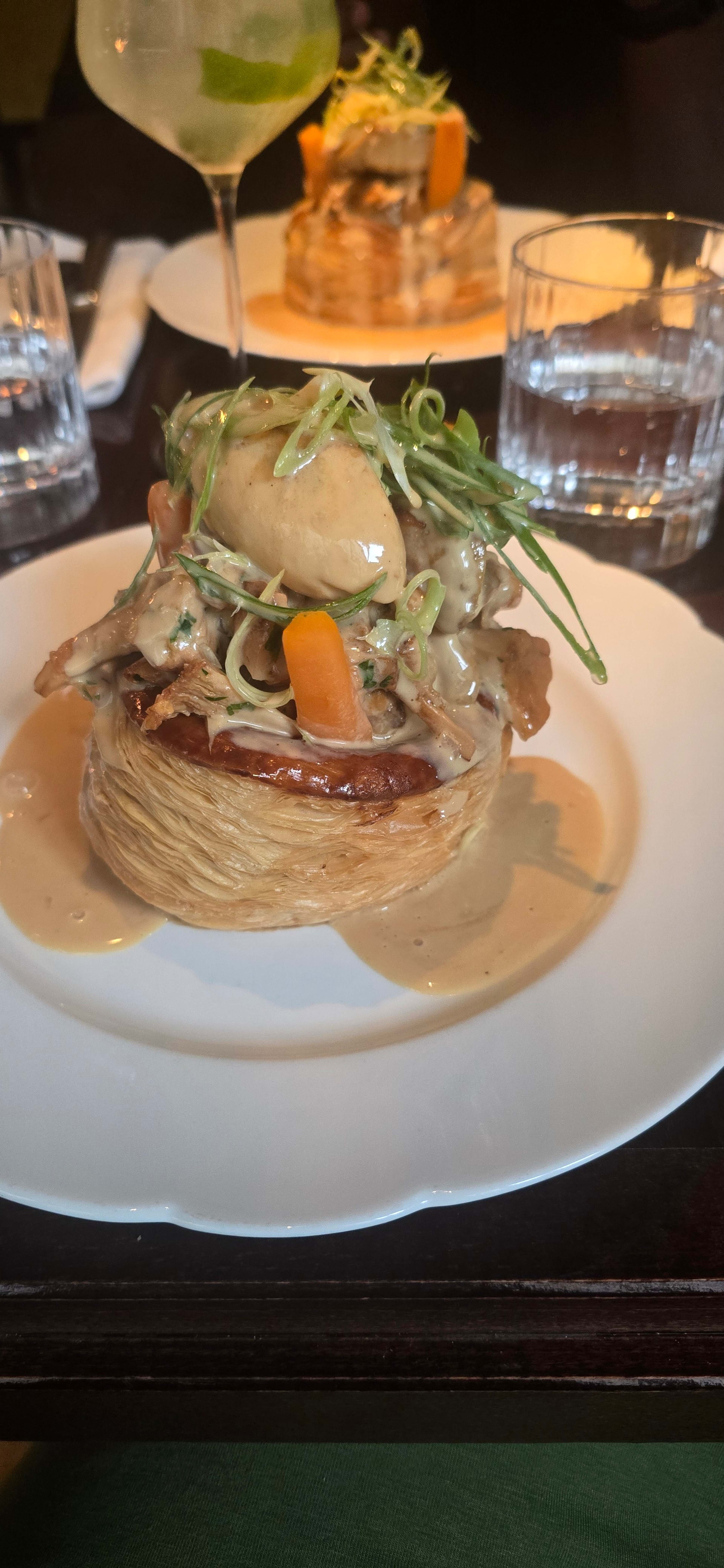 Coquille délicate garnie de morceaux tendres de viande, probablement de poulet, dans une sauce crémeuse, surmontée d'un œuf poché et décorée d'oignons verts et de légumes colorés.