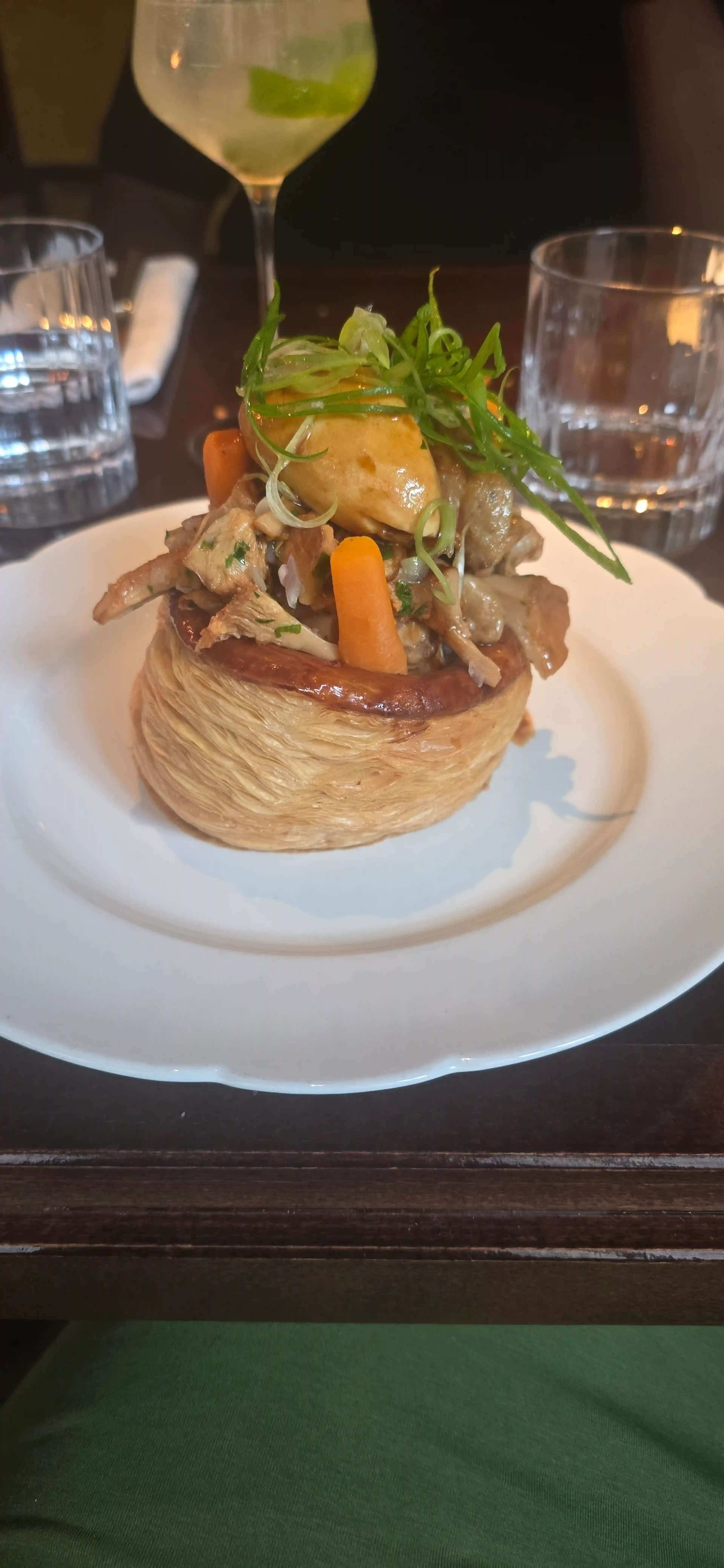 Plat joliment présenté avec une base de pâte feuilletée, garni de morceaux de poulet tendre, de légumes sautés et d'une purée ou sauce savoureuse orange. Décoré d'oignons verts frais et de petites carottes vives, offrant un contraste coloré.