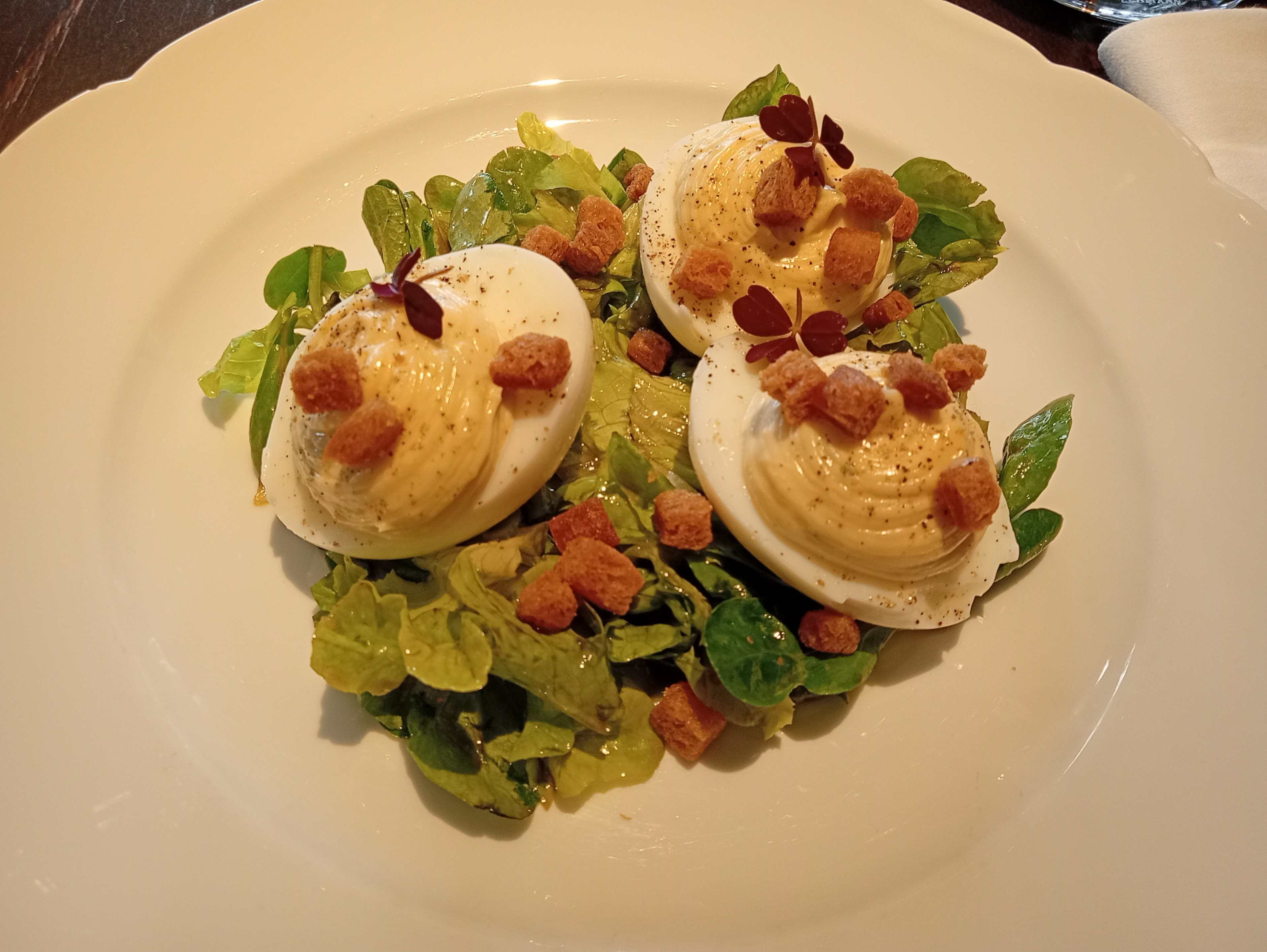 Assiette de trois œufs mimosa, garnis de paprika et de petits croûtons, servis sur un lit de jeunes pousses de salade, offrant un équilibre entre crémeux et croustillant.