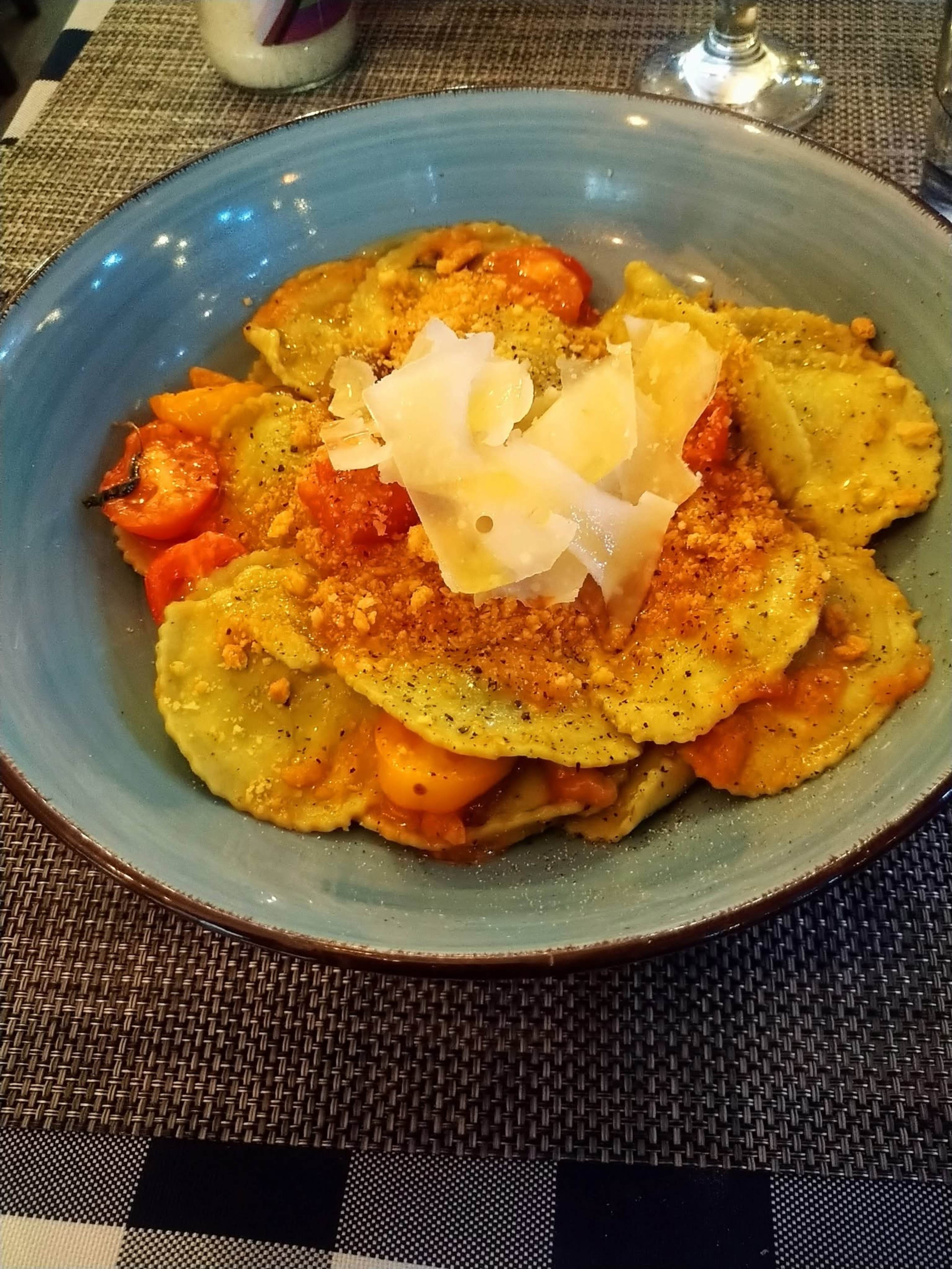 Assiette de raviolis farcis d'un mélange d'herbes vertes, garnis de miettes de pain grillées et de copeaux de fromage Parmesan, accompagnés d'une sauce aux notes d'orange, probablement à base de tomates séchées au soleil.