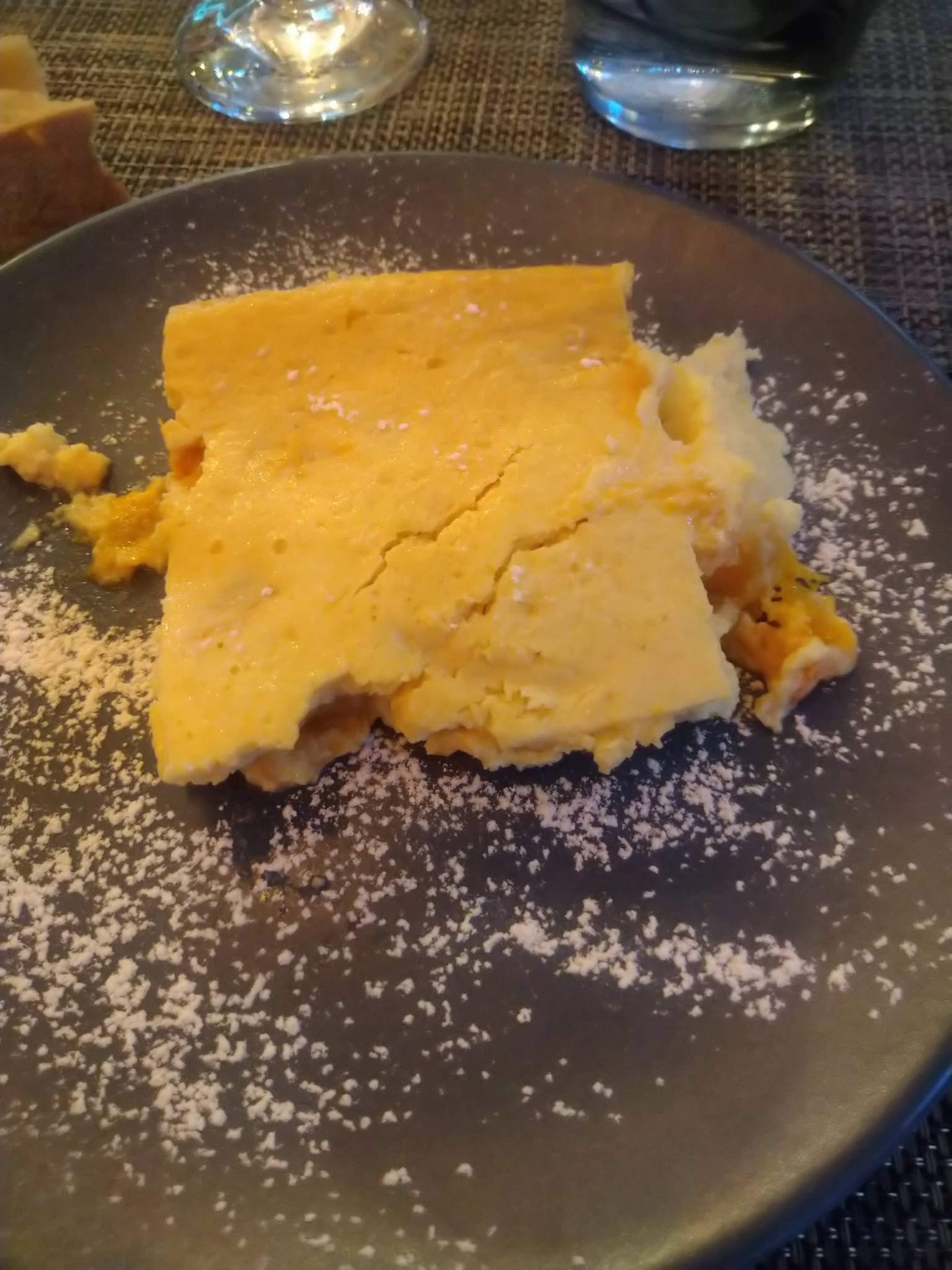 Une part de dessert, probablement un gâteau ou une crème anglaise, avec une texture lisse et crémeuse, saupoudrée de sucre glace et aux bords légèrement dorés, révélant un intérieur moelleux et une saveur riche.