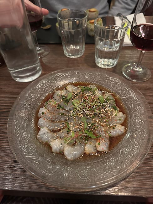 Plat de poisson cru finement tranché, assaisonné d'une sauce savoureuse, garni d'herbes fraîches et de graines de sésame.