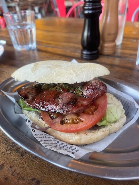 Sándwich abundante con salchicha a la parrilla, lechuga fresca y rodajas de tomate, todo en un pan suave y ligeramente tostado.