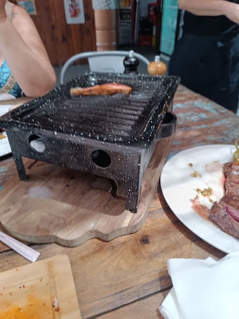 Parrilla de mesa con carne a la brasa y cortes adicionales, en un ambiente rústico y casual.