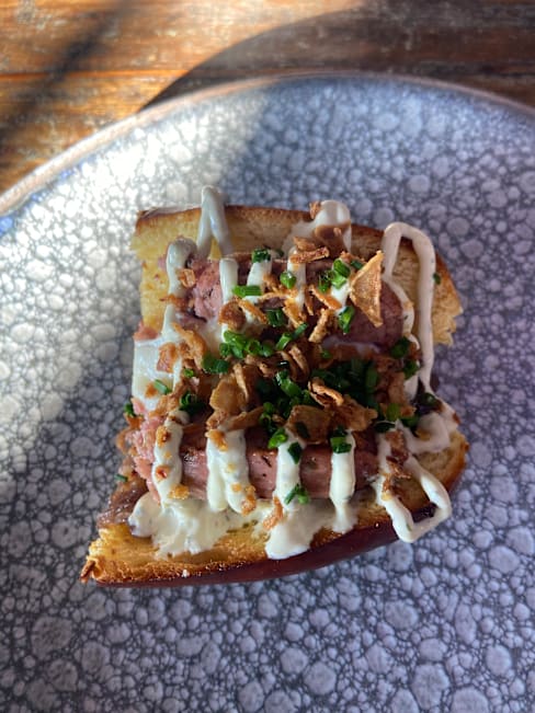 Tostada con carne picada a la parrilla, salsa cremosa, cebolla frita crujiente y cebollino fresco.