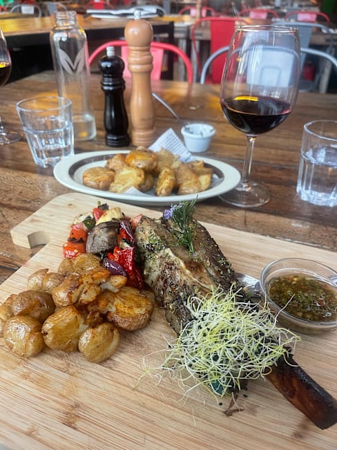 Carne de cordero asada con hierbas, acompañada de papas baby crujientes y verduras a la parrilla, servida con salsa verde.