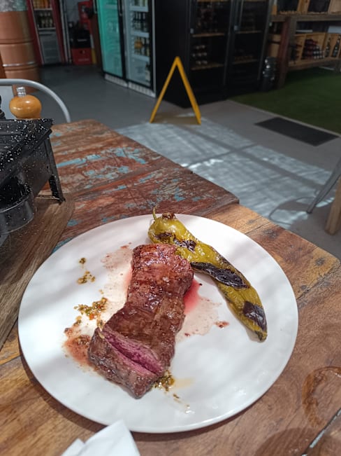 Un jugoso filete a punto medio, con un centro rojo-rosado y una costra marrón sabrosa, acompañado de un pimiento verde a la parrilla que aporta textura y un toque ahumado.