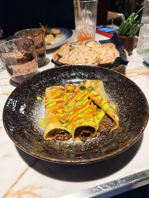 Assiette d'enchiladas roulées farcies d'une savoureuse préparation de viande effilochée et d'épices, nappées de sauces vertes et rouges, garnies d'herbes fraîches.
