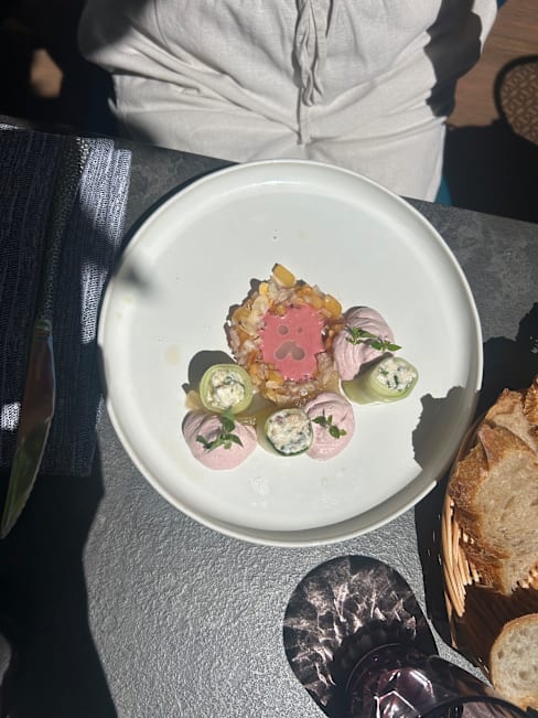 Plat artistique avec un mélange coloré d'ingrédients, comprenant un centre de fruits de mer et légumes finement hachés, entouré de délicates mottes de mélanges crémeux aux teintes pastel, garnies de jeunes pousses.