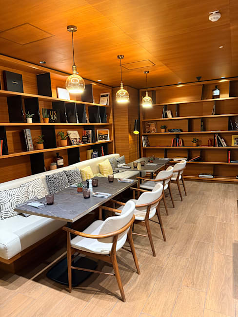 Intérieur de restaurant moderne avec des tons boisés chaleureux et un éclairage doux, comprenant un coin salon confortable et des étagères décoratives.