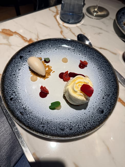 Dessert joliment présenté avec une base de chocolat, crème fouettée délicate, glace lisse, coulis de fruits colorés et biscuits émiettés pour une texture croquante.