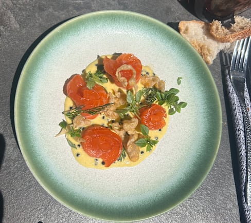 Plat élégamment présenté avec des tranches de tomates rôties sur une sauce crémeuse jaune, agrémenté de morceaux croustillants et d'herbes fraîches.