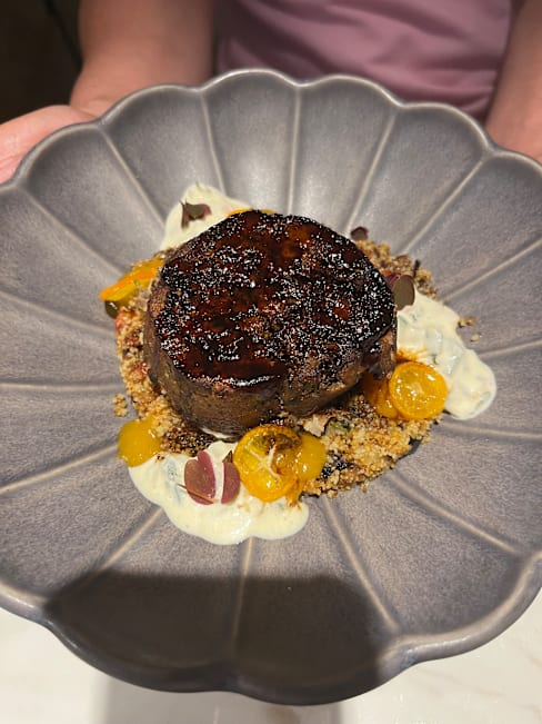 Plat élégamment présenté avec un morceau de viande parfaitement cuit, servi sur un lit de grains texturés, accompagné de petites touches d'une sauce crémeuse et de tranches de fruit jaune, apportant douceur et couleur.