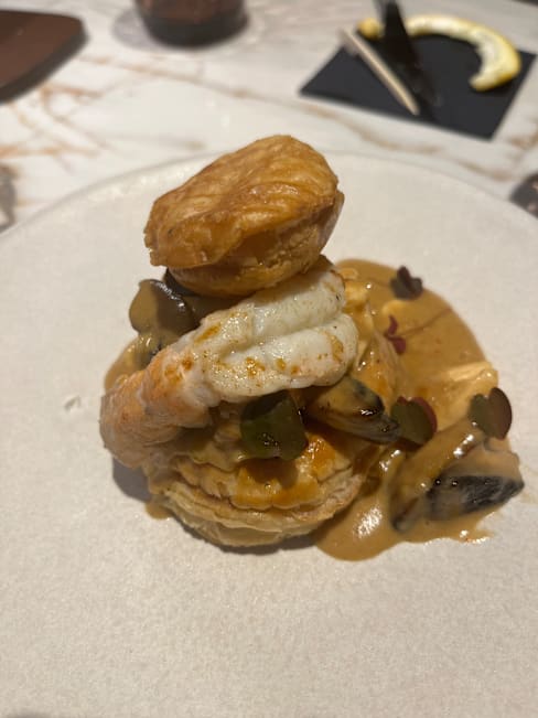 Plat en couches avec une pâte feuilletée croustillante à la base, garni de crevettes tendres et d'une sauce crémeuse légèrement sucrée, agrémenté de petits morceaux de légumes pour une présentation élégante.