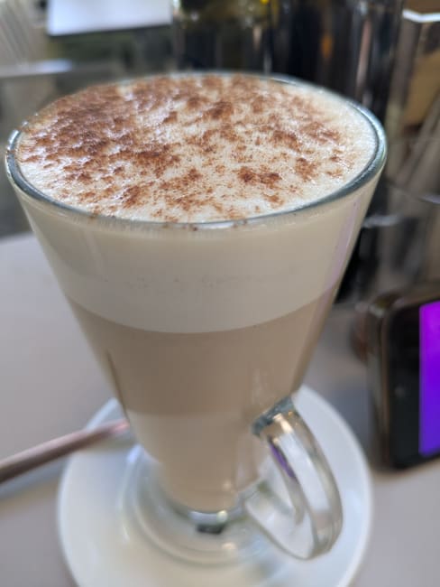 Latte cremoso con espuma de leche y un toque de cacao en polvo, que presenta un color marrón cálido y capas distintivas de café y leche.
