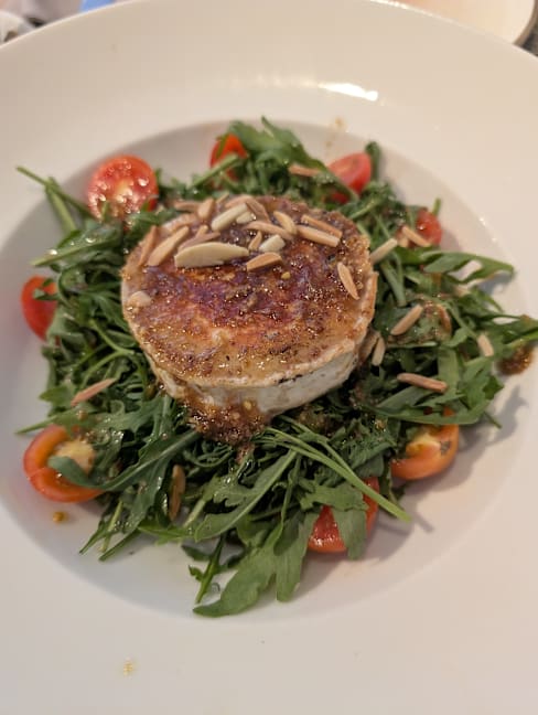 Queso de cabra a la parrilla sobre una cama de rúcula fresca, acompañado de tomates cherry y almendras laminadas.