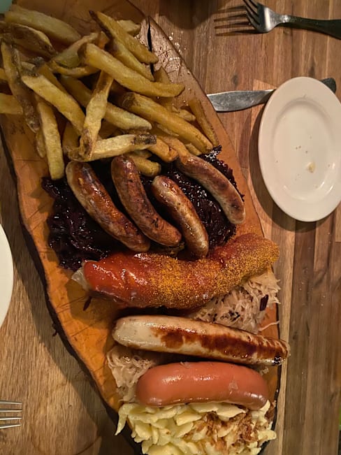Plateau en bois avec un assortiment de saucisses, dont une bratwurst grillée et une saucisse épicée, accompagnées de frites dorées et croustillantes, ainsi que de choucroute acidulée, le tout rehaussé d'une touche de moutarde.