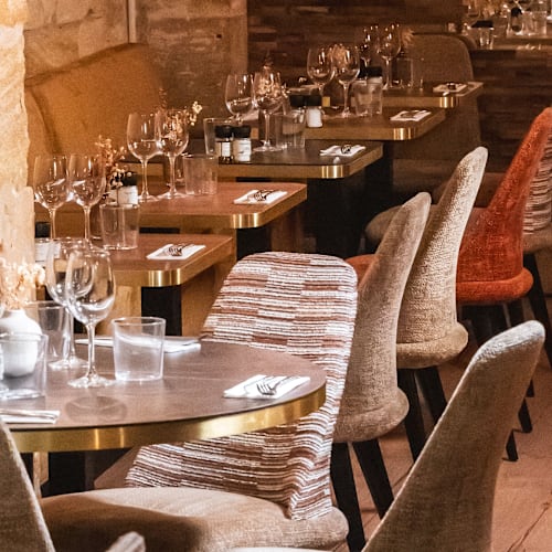 Intérieur de restaurant chaleureux avec des tables élégamment disposées, des chaises confortables et des murs en pierre naturelle, créant une ambiance sophistiquée et accueillante.