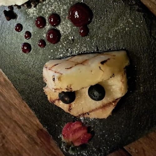 Queso a la parrilla con salsa de bayas oscuras, arándanos frescos y una rodaja de fresa.