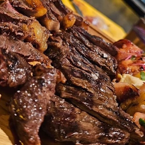 Plato de carnes a la parrilla, con un gran filete jugoso y cortes de pollo o cerdo, acompañado de verduras asadas y hierbas frescas.