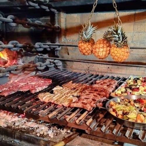 Escena de barbacoa con carnes asadas y verduras a la parrilla, incluyendo pimientos, calabacines y cebollas, todo con un toque ahumado y caramelizado.