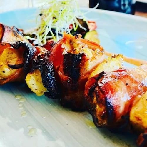 Brochetas de pollo jugoso envuelto en tocino crujiente, adornadas con brotes frescos.