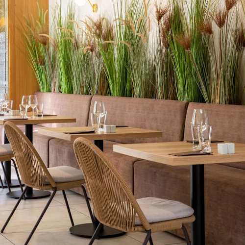Intérieur de restaurant moderne avec un agencement de sièges confortable, décoré de verdure luxuriante et de tables en bois clair, créant une ambiance accueillante et élégante.