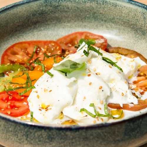 Assortiment coloré de tomates tranchées, surmonté de burrata crémeuse, garni d'herbes fraîches et arrosé d'huile d'olive.