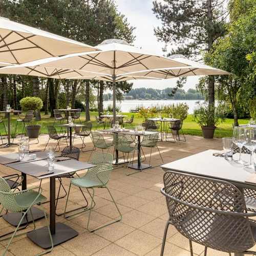 Espace de restauration en plein air avec des tables sous de grands parasols, entourées de chaises vertes, offrant une atmosphère tranquille et pittoresque.