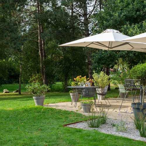 Espace de restauration en plein air dans un environnement verdoyant, avec des tables et des chaises confortables, ombragées par de grands parasols, offrant une atmosphère paisible pour des repas en plein air.