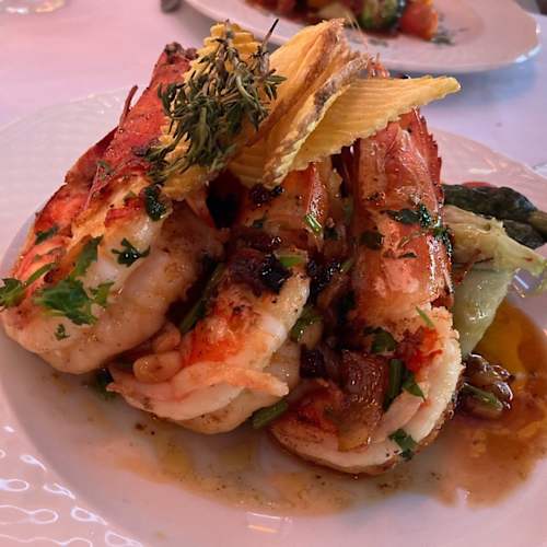 Prato elegantemente apresentado com grandes camarões suculentos grelhados, guarnecidos com ervas frescas, acompanhados de espargos tenros e uma mistura de legumes salteados, regados com um molho saboroso.