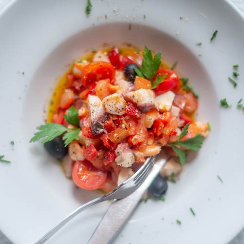 Salada fresca com tomates, pepinos e pimentos em cubos, acompanhada de pedaços de frango grelhado e azeitonas pretas, guarnecida com salsa e regada com um molho leve.