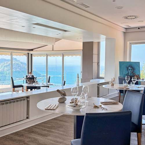 Interior de restaurante moderno y minimalista, con grandes ventanales que ofrecen vistas al océano y una atmósfera sofisticada y acogedora.