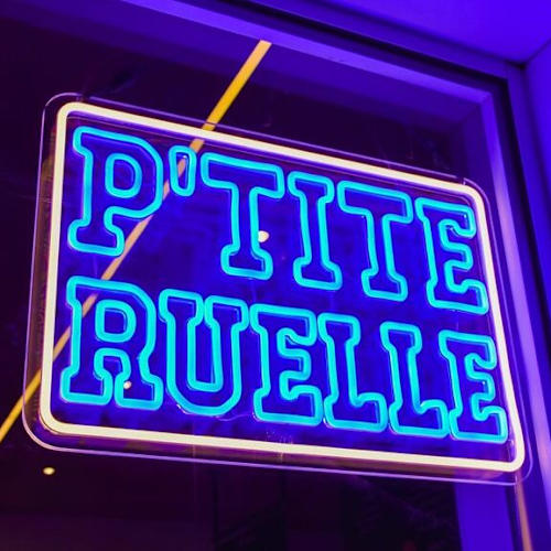 Enseigne au néon "P'tite Ruelle" en lettres bleues, créant une ambiance moderne et accueillante pour un restaurant ou café.