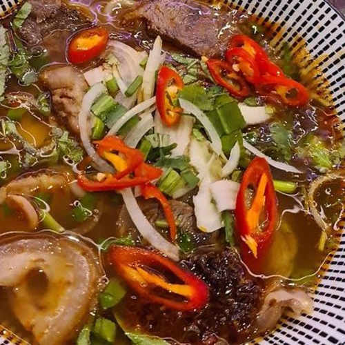 Bol de bouillon savoureux avec des tranches de viande tendre, des herbes, des oignons verts frais et des morceaux de tripes, offrant une texture copieuse.