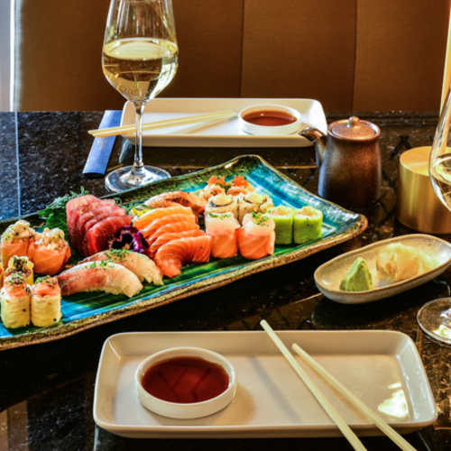 Seleção de sushi disposta de forma elegante, incluindo nigiri com fatias de peixe fresco como salmão e atum, além de rolos coloridos com abacate, pepino e caranguejo, acompanhados de molho de soja e wasabi.