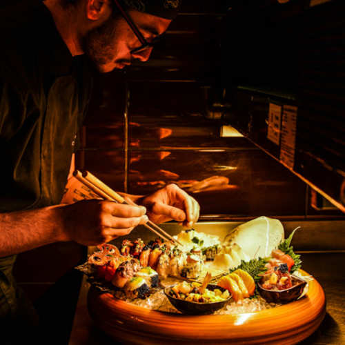 Prato de sushi com uma variedade de rolos decorados com abacate, peixe delicado e ovas laranja, acompanhado de sashimi fresco e guarnições de rabanete e microverdes.