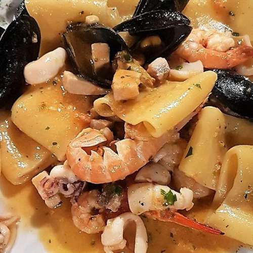 Pasta pappardelle con frutti di mare, gamberi, cozze e calamari, condita con una leggera salsa dorata e arricchita da erbe fresche.