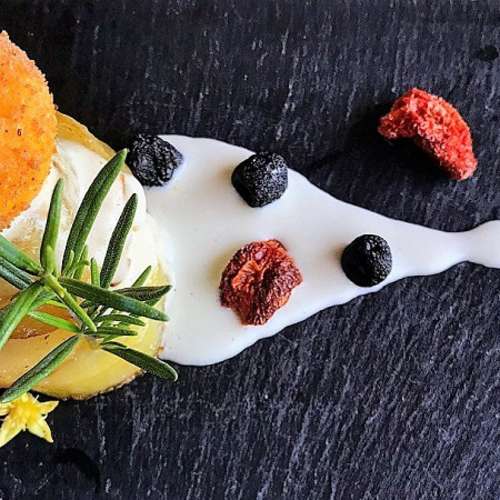 Crocchetta dorata su un letto di patate affettate, guarnita con salsa bianca, erbe fresche e fiori edibili, accompagnata da pezzi di frutta secca.