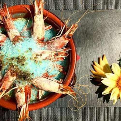 Gamberi freschi disposti su un letto di ghiaccio tritato, guarniti con erbe delicate e fiori edibili.