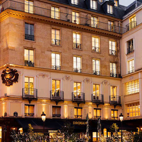Extérieur charmant d'un restaurant avec une architecture classique, des grandes fenêtres, des balcons en fer forgé et une ambiance accueillante, entouré de verdure.
